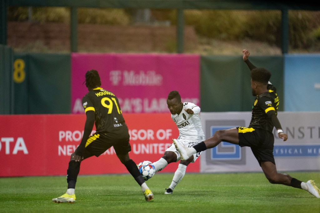 Las Vegas Lights FC forward Soloman Asante shooting the ball through two New Mexico United players