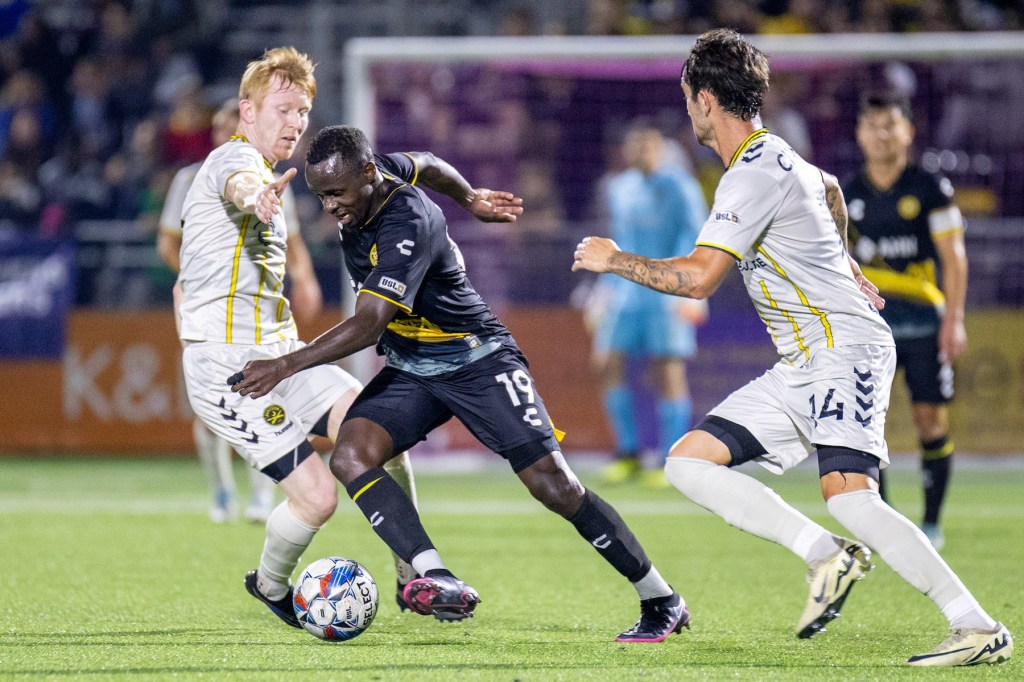 Hounds forward Edward Kizza dribbles between a pair of Charleston Battery defenders in the team's 2-0 win at Highmark Stadium.