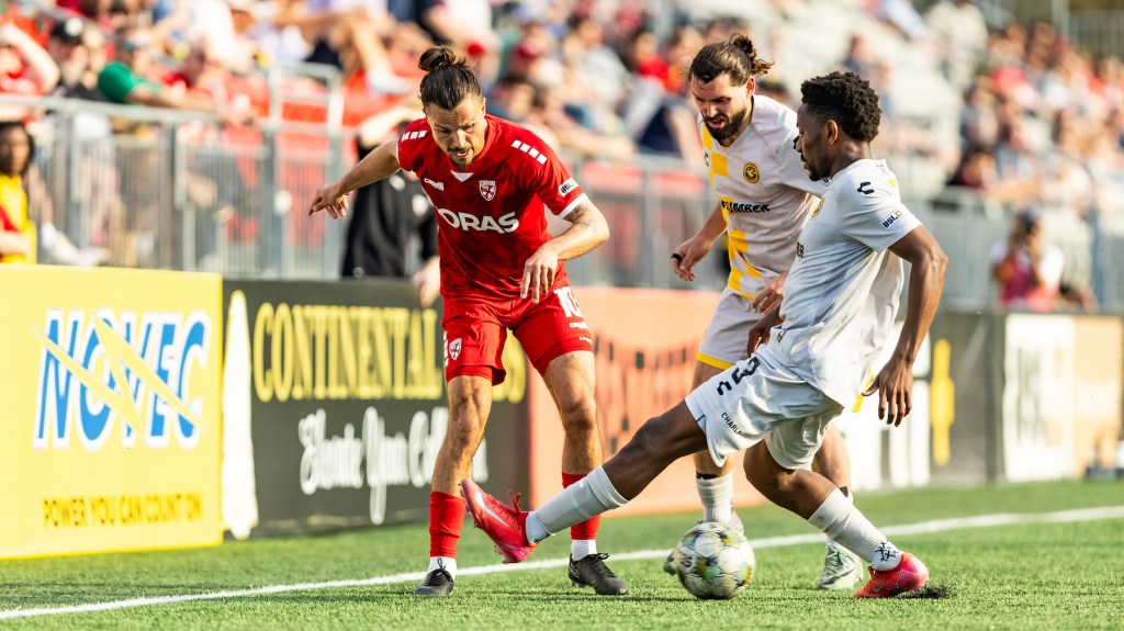 Pittsburgh Riverhounds Perrin Barnes (right) and Jackson Walti surround Loudoun United FC's Florian Valot during the teams' match April 19, 2025 at Segra Field in Leesburg, Va. (Photo: Mallory Neil/Riverhounds SC)